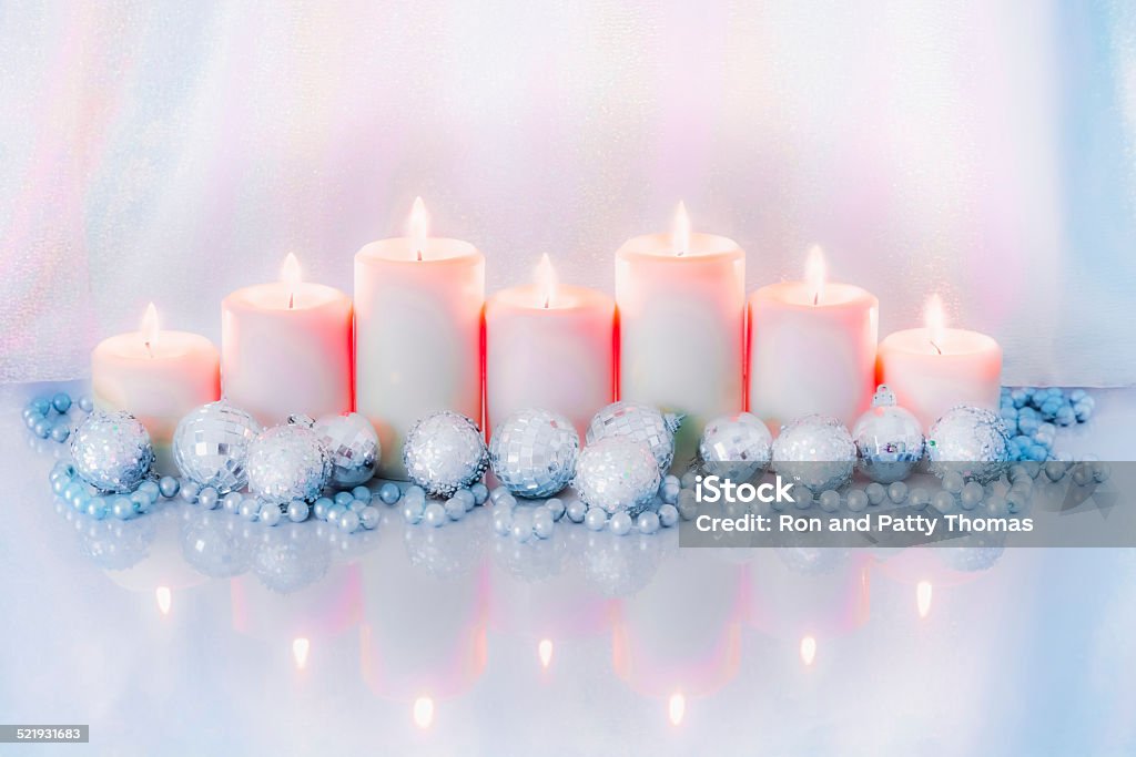 Seven Christmas candles and ornaments in blue and pink (P) Seven  decorated candles glow and are reflected, with the decorations, in a shiny surface, all in tones of opalescent blue and pink, for Christmas or for a romantic event. Anniversary Stock Photo