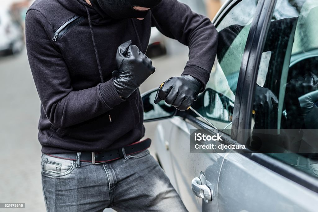Car thief, car theft The man dressed in black with a balaclava on his head trying to break into the car. He uses a screwdriver. Car thief, car theft concept Stealing - Crime Stock Photo