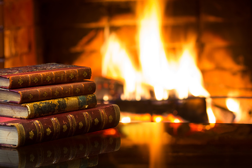 Antique books in front of warm fireplace. Magical relaxed cozy atmosphere near fire.