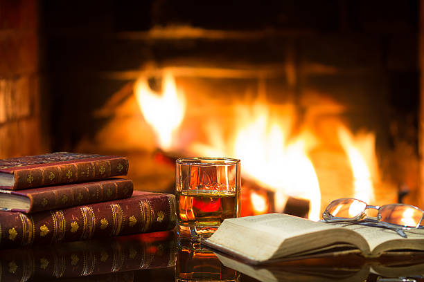istock Glass alcoholic drink wine antique books in front warm fireplace. 521977090