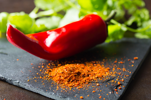 Ground dry red pepper on stone board with fresh chili on background. Closeup