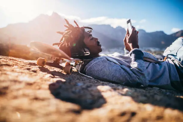 Photo of African American Skater Resting and Looking at Smartphone at Sea