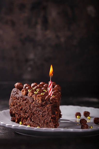 istock Piece of chocolate cake with candle on a dark background 521985390