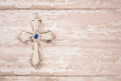 Silver metal cross on rustic wooden surface.  The cross is beautifully designed in with delicate details.  Jewelry.  Christianity, religion.