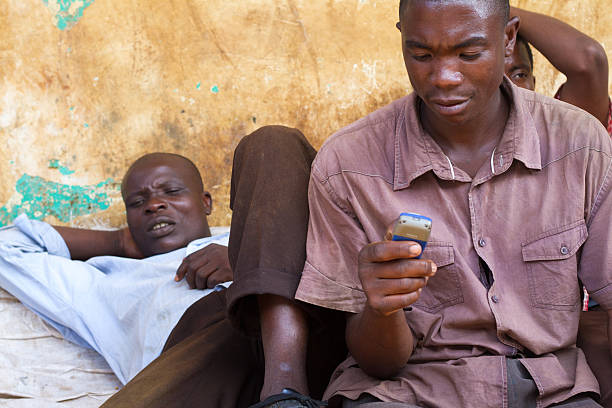 Mwanza, Tanzania: Men Relaxing, One with Cell Phone Mwanza, Tanzania - May 8, 2012: Men relaxing outside on the street in central Mwanza--one lying down, one looking at his phone. mwanza city tanzania stock pictures, royalty-free photos & images