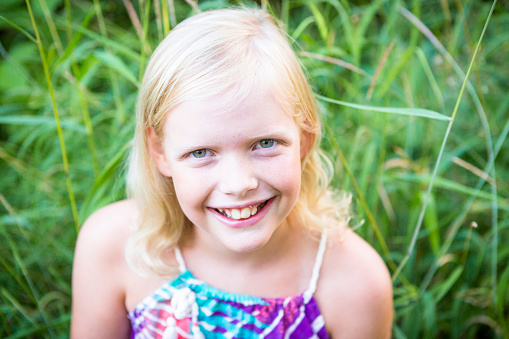 Blonde girl smiling and looking up into camera with grass in background.