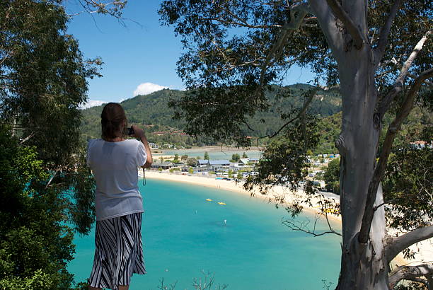 Woman takes a photo from viewpoint at Kaiteriteri, Tasman, NZ A woman takes a photo of a view of Kaiteriteri Beach, gateway to the Abel Tasman National Park, in the Tasman Region, New Zealand. nelson city new zealand stock pictures, royalty-free photos & images