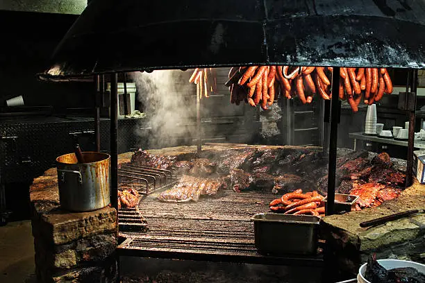 Sausages hanging over brisket smoking over a large BBQ pit.
