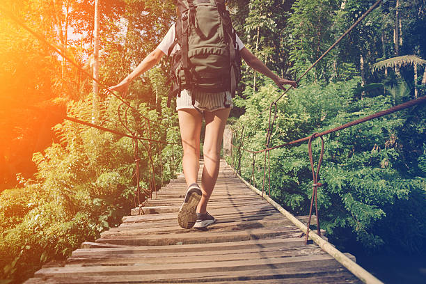 istock Young woman with backpack balancing across hanging bridge 522000036