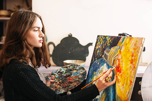 Creative pensive  painter paints a colorful picture. Creative process of creating abstract painting in art workroom. Closeup. Creative positive woman painter paints in her studio abstract picture. 