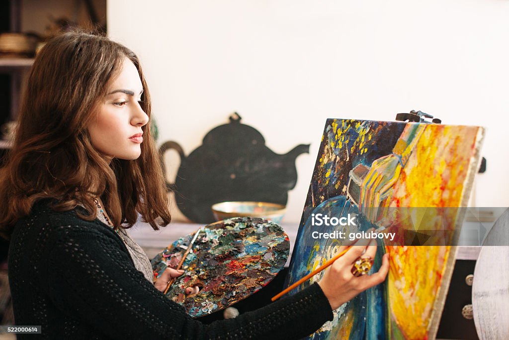 The creative process of creating abstract painting Creative pensive  painter paints a colorful picture. Creative process of creating abstract painting in art workroom. Closeup. Creative positive woman painter paints in her studio abstract picture.  Artist Stock Photo