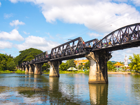 Kanchanaburi, Thailand - August 12, 2014: The historical River Kwai Bridge in Kanchanaburi, Thailand. People can be seen crossing the bridge and taking photos as part of a tour group.