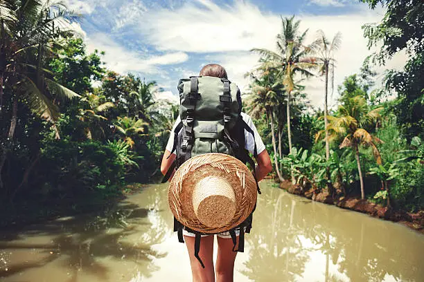 Traveler woman with backpack standing near big tropical river at sunny day