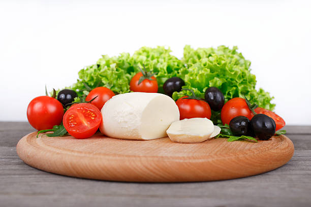 mozzarella with cherry tomatoes, arugula, lettuce leaves and bla mozzarella cheese with cherry tomatoes, arugula, lettuce leaves and black olives on on a round wooden board  on wooden table closeup on white background buffalo iowa stock pictures, royalty-free photos & images