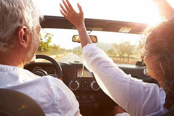 Mature Couple Driving Along Country Road In Open Top Car Mature Couple Driving Along Country Road In Open Top Car Hoding Arms Up convertible photos stock pictures, royalty-free photos & images