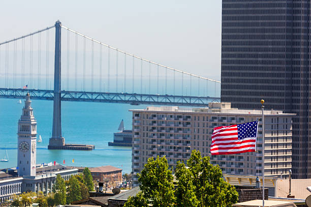 usa, amerikanische flagge san francisco bay bridge und den clock tower - san francisco county embarcadero center bay bridge built structure stock-fotos und bilder