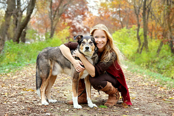 Woman and Dog in Autumn Woods on Walking Trail A thirty year old woman is stopping to hug her German Shepherd dog as they are walking through the fallen leaves in the woods on an Autumn day. rescued dog stock pictures, royalty-free photos & images