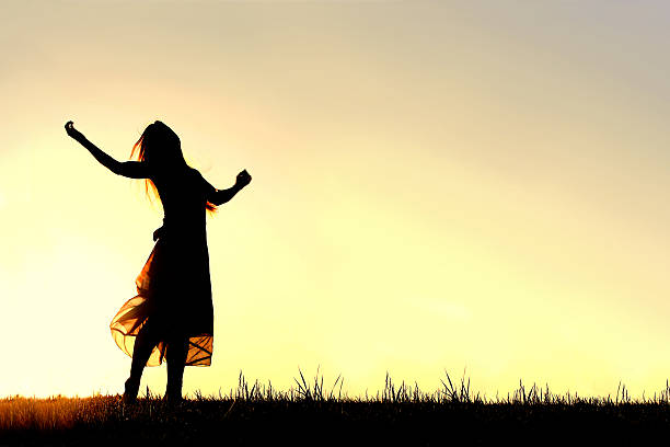 Silhouette of Woman Dancing and Praising God at Sunset A woman wearing a long skirt, with long blonde hair, is dancing and praising God, while silhouetted against the evening sky ballerina shadow stock pictures, royalty-free photos & images