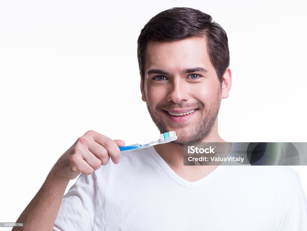 Smiling young man with a toothbrush. Portrait of a smiling young man with a toothbrush in a white t-shirt -  isolated on white. Adult Stock Photo