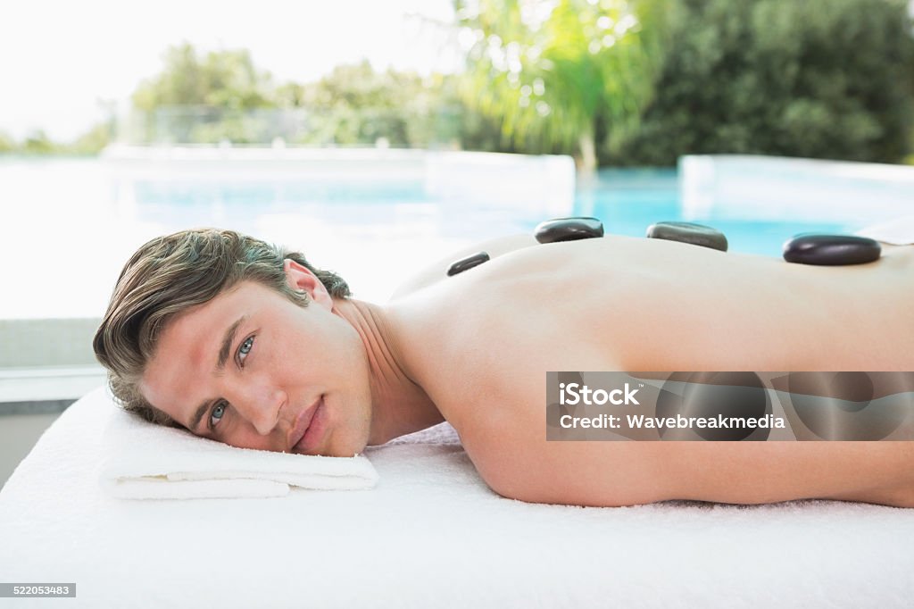 Handsome man receiving stone massage at spa center Side view of a handsome young man receiving stone massage at spa center 20-29 Years Stock Photo