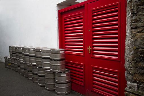 Stacked kegs of beer outside a red door in Ireland. Copy space on the white wall.