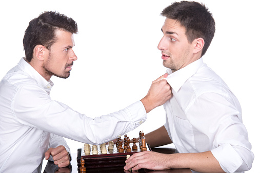 Portrait of two young man are playing chess on the white background. Should play by the rules.