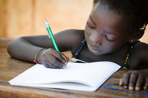 A young African girl writing her lesson on a sheet of paper.