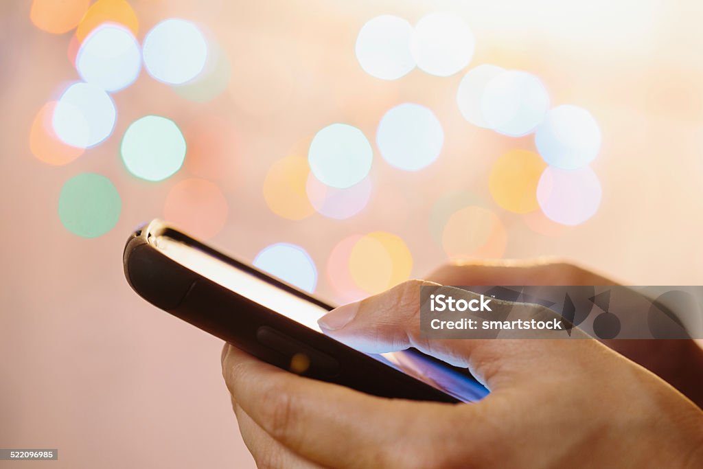 Closeup of woman using thumbs to type on mobile phone Closeup of woman's hands texting on a smartphone with defocused lights in the background. Close-up Stock Photo