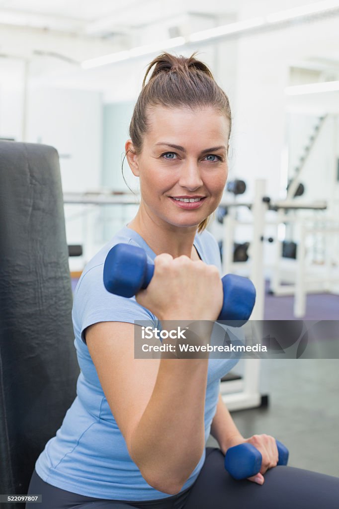 Fit brunette lifting blue dumbbells Fit brunette lifting blue dumbbells at the gym Blue Stock Photo