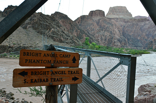 Trail Signs pointing the way for Bright Angel Camp, Phantom Ranch, Bright Angel Trail and South Kaibab Trail at the South end of the Siver Bridge which spans the Colorado River at the bottom of Grand Canyon National Park, Arizona, USA.