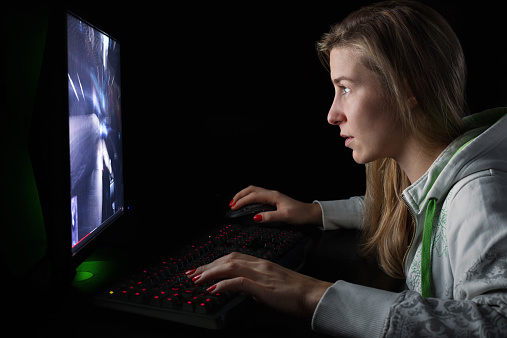 Gamer girl playing first person shooter game on high end pc, isolated on a black background