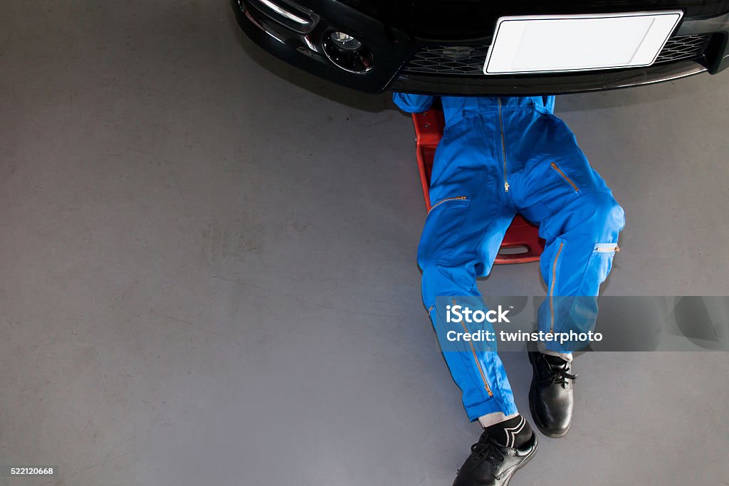 Mechanic in blue uniform lying down and working under car Mechanic in blue uniform lying down and working under car at the garage. Auto Repair Shop Stock Photo