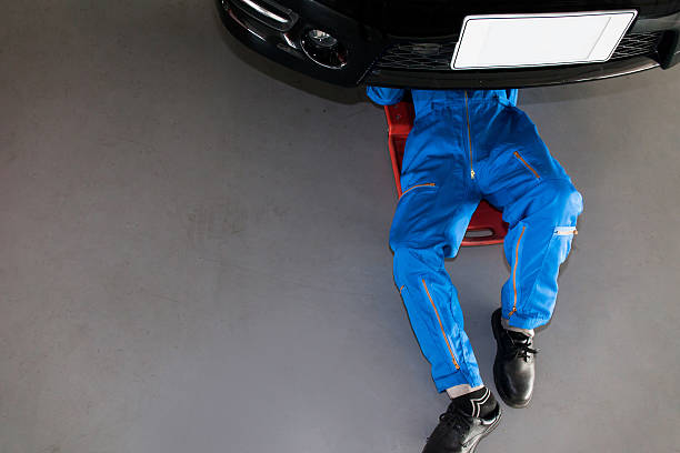 Mechanic in blue uniform lying down and working under car Mechanic in blue uniform lying down and working under car at the garage. mechanic working under car stock pictures, royalty-free photos & images