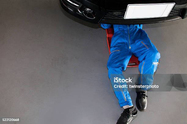 Mechanic In Blue Uniform Lying Down And Working Under Car Stock Photo - Download Image Now