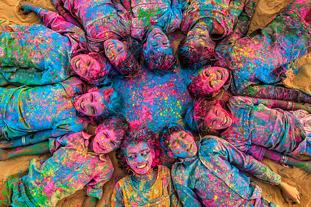 Group of happy Indian children playing holi, desert village, India Group of happy Gypsy Indian children playing happy holi on sand dunes in desert village, Thar Desert, Rajasthan, India. Children are lying in a circle. Color powders are on their faces and clothes. Holi is a religious festival in India, celebrated, with the color powders, during the spring. holi stock pictures, royalty-free photos & images