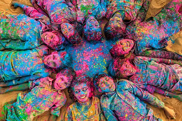 Group of happy Gypsy Indian children playing happy holi on sand dunes in desert village, Thar Desert, Rajasthan, India. Children are lying in a circle. Color powders are on their faces and clothes. Holi is a religious festival in India, celebrated, with the color powders, during the spring.