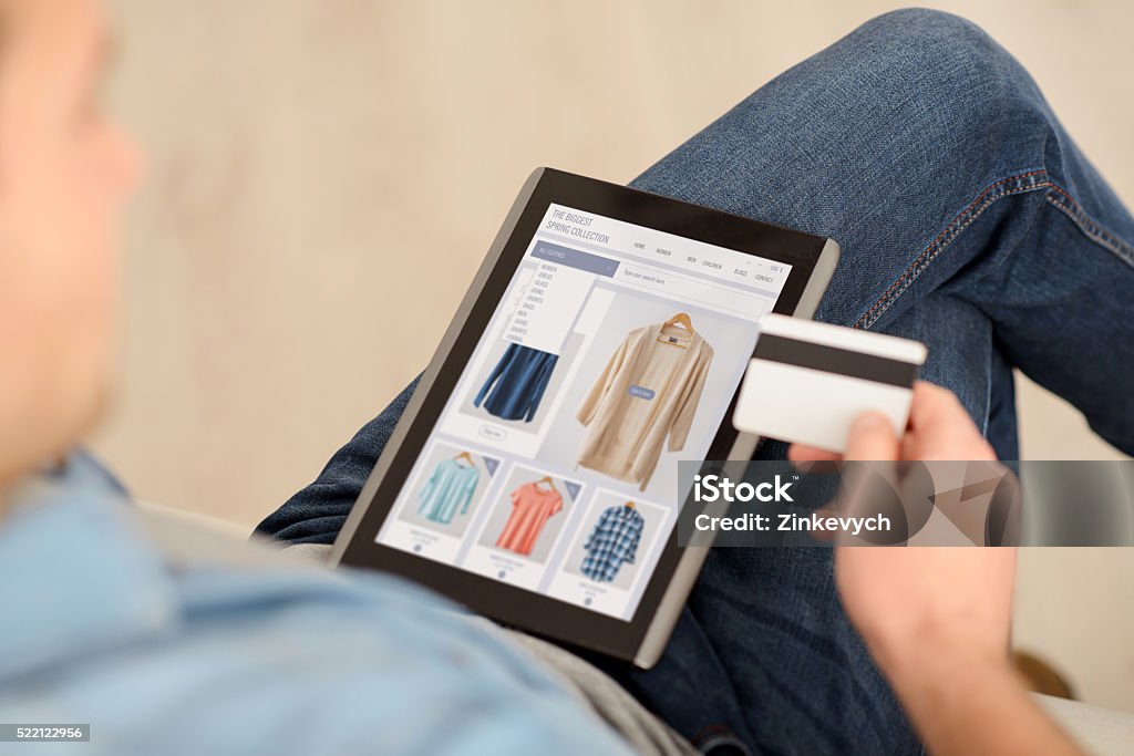 Pleasant man using tablet Pay it off. Pleasant man sitting on the couch and holding credit card while using tablet  Online Shopping Stock Photo