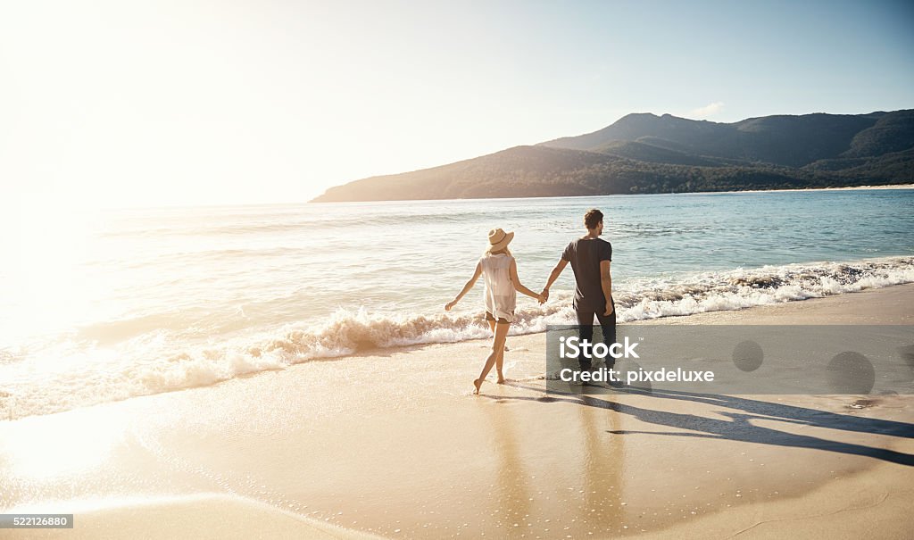 Treating themselves to a beachside vacation Shot of a young couple going for a stroll along the beach Beach Stock Photo
