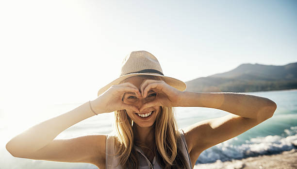 I heart summer! Shot of a young woman making a heart shaped gesture with his hands on a day at the beach only young women stock pictures, royalty-free photos & images