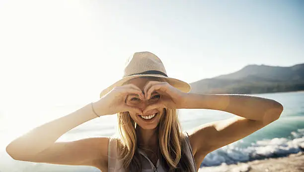 Shot of a young woman making a heart shaped gesture with his hands on a day at the beach