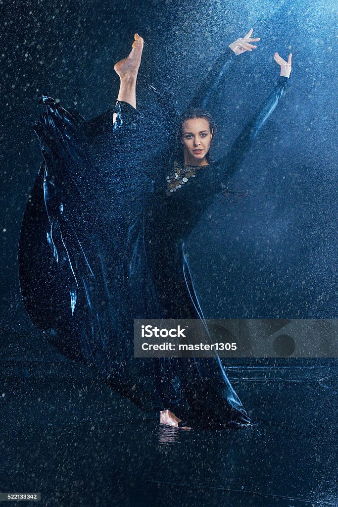 The young beautiful modern dancer dancing under water drops The young beautiful modern dancer in long dress dancing under water drops in blue aqua studio  Activity Stock Photo