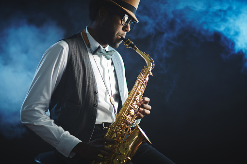 Elegant jazzman playing sax with smoke on background