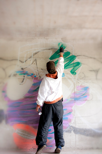 Graffiti artist drawing graffiti and reaching for the highest point of his graffiti piece.