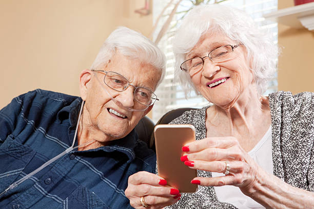 Senior Couple Looking At Smart Phone An 88 year old woman and her 91 year old husband smiling as they look at a smart phone that she is holding. medical oxygen equipment stock pictures, royalty-free photos & images