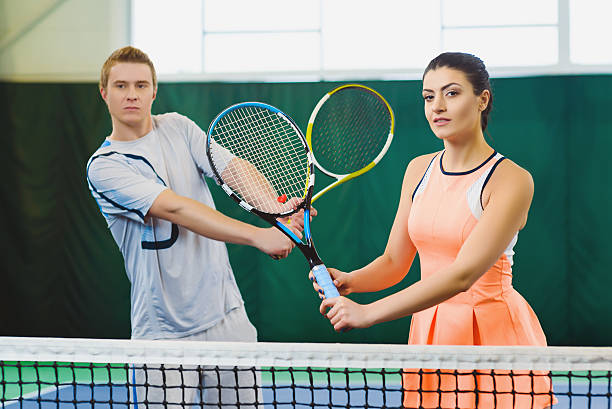 Mixed Doubles player hitting tennis ball, partner standing near net stock photo