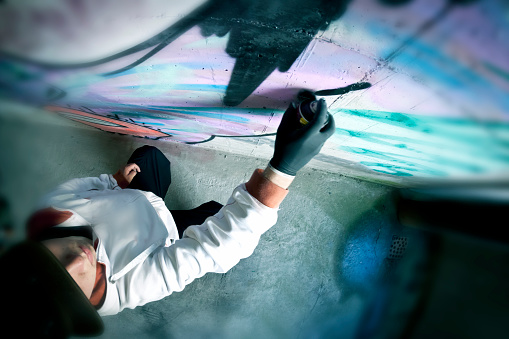 Young graffiti artist drawing graffiti on concrete wall, high angle view.