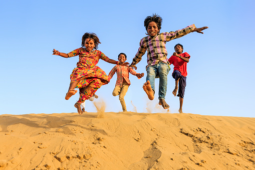 Group of happy Indian children jumping off  a dune into sand - desert village, Thar Desert, Rajasthan, India.