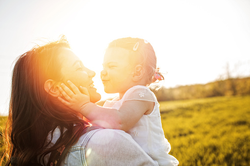 Smiling mother and her baby girl on a field on a bright sunny day