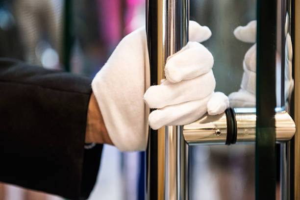 Doorman with White Gloves Opening Door at Luxury Shopping Mall Unrecognizable doorman with white gloves holds a brass handle to a glass door at an expensive hotel, store or mall in Kowloon, Hong Kong, China. bellhop stock pictures, royalty-free photos & images