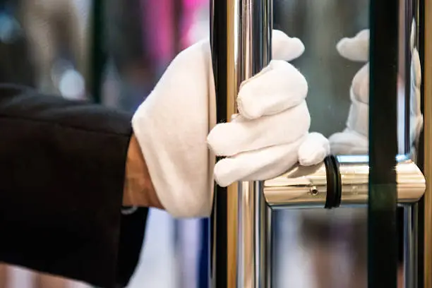 Unrecognizable doorman with white gloves holds a brass handle to a glass door at an expensive hotel, store or mall in Kowloon, Hong Kong, China.